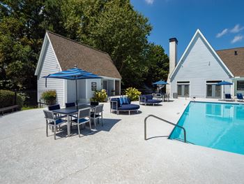 a swimming pool with a table and chairs next to a house with a chimney